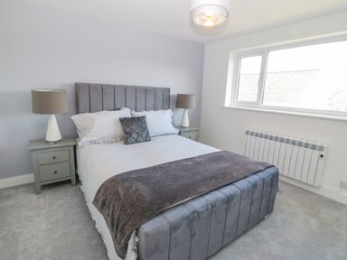 A bedroom with a double bed a grey headboard and footboard two bedside tables with lamps and a window at Daresfield in Cemaes Bay