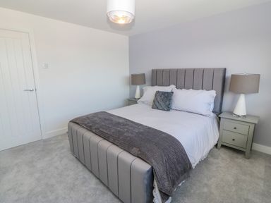 A bedroom with a bed a gray blanket and two bedside tables with lamps at Daresfield in Cemaes Bay