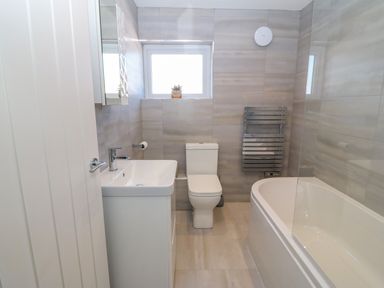 A bathroom with a sink cabinet toilet bathtub window and heated towel rail at Daresfield in Cemaes Bay