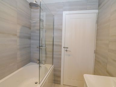 A bathroom with a bathtub shower combination glass shower screen a white door and a white sink at Daresfield in Cemaes Bay
