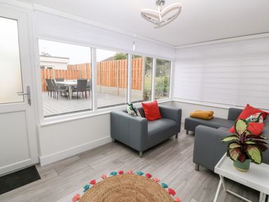 A sunroom with gray armchairs and a sofa with red and patterned cushions a round jute rug and a white side table with a potted plant at Daresfield in Cemaes Bay