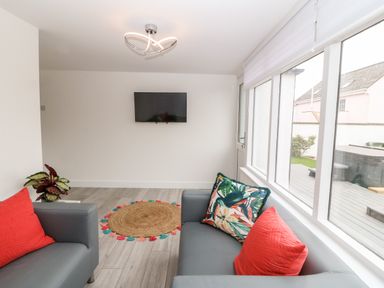 A sitting room with two grey sofas with red and patterned cushions a round woven rug mounted television and large windows at Daresfield in Cemaes Bay