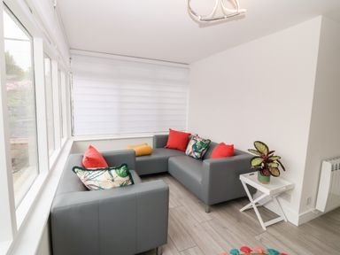 A sitting area with a grey L-shaped sofa with colorful cushions and a white side table with a potted plant at Daresfield in Cemaes Bay