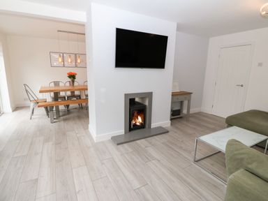 A sitting area with a wall mounted television and fireplace next to a dining area with a wooden table and metal chairs at Daresfield in Cemaes Bay