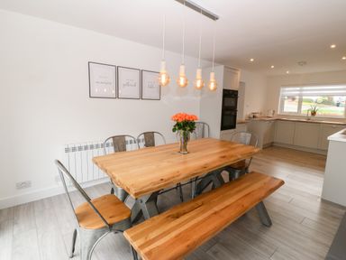 A dining area with a wooden table and bench metal chairs and hanging light bulbs in a kitchen at Daresfield in Cemaes Bay
