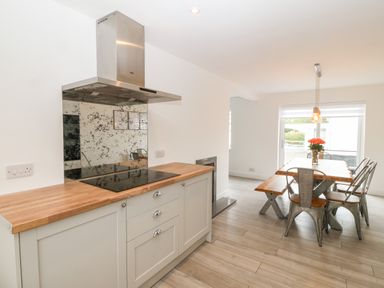 A kitchen area with a stovetop and hood next to a dining area with a wooden table bench and metal chairs at Daresfield in Cemaes Bay