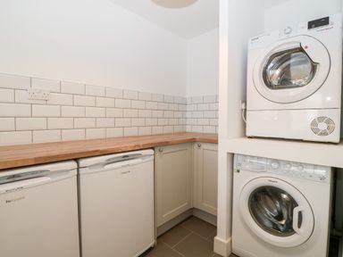 A utility room with two washing machines stacked and two refrigerators under a wooden countertop at Daresfield in Cemaes Bay