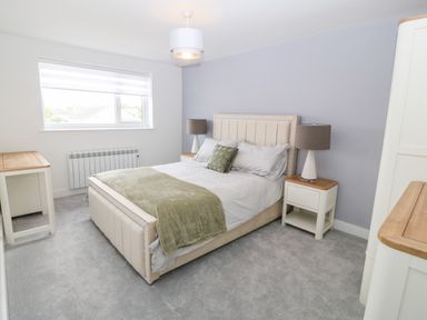 A bedroom with a bed with green blanket and pillows bedside tables lamp and window at Daresfield in Cemaes Bay