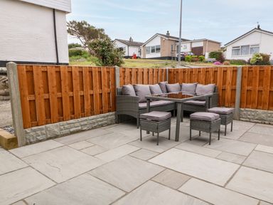 An outdoor patio area with a corner sofa an outdoor table and three stools surrounded by a wooden fence at Daresfield in Cemaes Bay