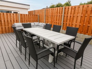 An outdoor patio with a white table surrounded by black chairs and a gray cushioned corner sofa at Daresfield in Cemaes Bay
