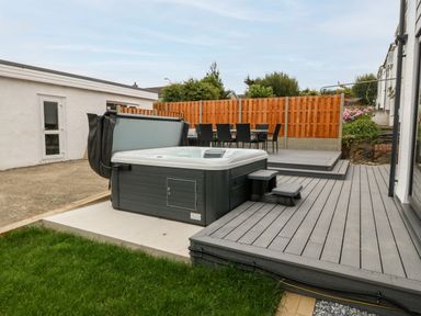 An outdoor area with a hot tub on a gray deck and a dining table with chairs behind a wooden fence at Daresfield in Cemaes Bay