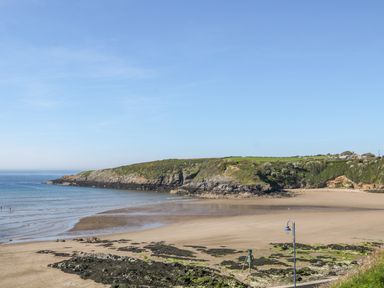 A sandy beach with rocky areas and a grassy cliff in the background under a clear sky at Daresfield in Cemaes Bay