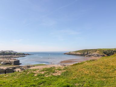 A coastal view with a sandy beach green grassy area rocky cliffs and a boat in the water at Daresfield in Cemaes Bay