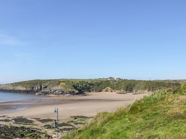 A sandy beach with rocky cliffs and green grass under a clear blue sky at Daresfield in Cemaes Bay