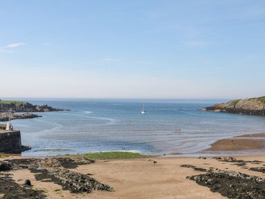 A beach with people and a boat in the water at Daresfield in Cemaes Bay