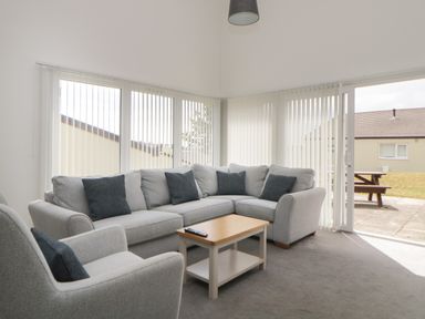 A sitting room with a grey corner sofa and armchair with cushions a wooden coffee table and vertical blinds on windows at Harcombe House Bungalow 11 in Chudleigh
