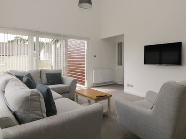 A living room with a grey sofa set a wooden coffee table and a wall-mounted television at Harcombe House Bungalow 11 in Chudleigh