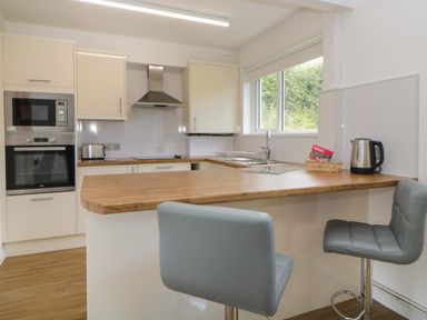 A kitchen with cream cabinets wooden countertops a built-in oven microwave toaster kettle and two gray bar stools at Harcombe House Bungalow 11 in Chudleigh