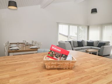 A dining area with a wooden table set with plates and glasses next to a living room with a grey sectional sofa and a wooden coffee table at Harcombe House Bungalow 11 in Chudleigh