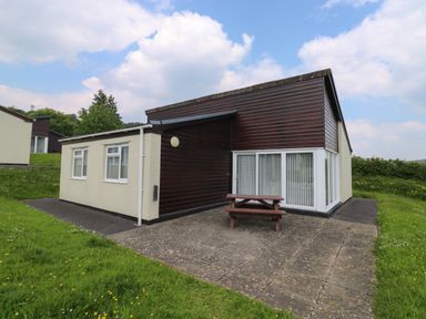 A bungalow with a patio and picnic table on a grassy lawn at Harcombe House Bungalow 11 in Chudleigh