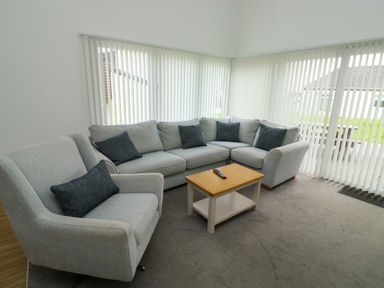 A living room with a grey armchair and an L shaped sofa with dark cushions and a wooden coffee table with a remote at Harcombe House Bungalow 11 in Chudleigh