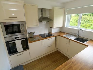 A kitchen with built in oven and microwave wooden countertops electric stove and a window above a sink at Harcombe House Bungalow 11 in Chudleigh