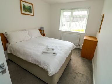 A bedroom with a double bed bedside lamp chest of drawers and a window with vertical blinds at Harcombe House Bungalow 11 in Chudleigh