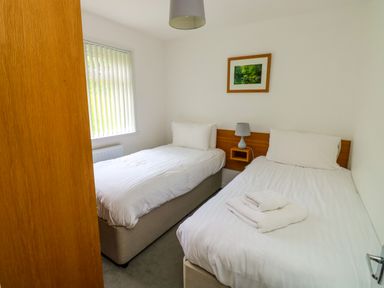 A bedroom with two single beds white bedding and a lamp on a wooden headboard at Harcombe House Bungalow 11 in Chudleigh