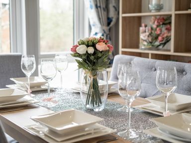 A dining table set with white square plates and wine glasses with a flower centerpiece at Loluke Lodge on The Lake 5 Coniston Drive Borwick near Carnforth