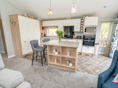 A kitchen with an island and two stools next to a window at Loluke Lodge on The Lake 5 Coniston Drive Borwick near Carnforth