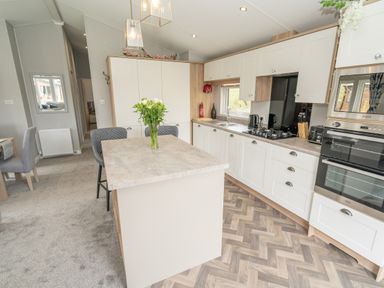A kitchen with an island with flowers and chairs and built in cabinets and appliances at Loluke Lodge on The Lake 5 Coniston Drive Borwick near Carnforth