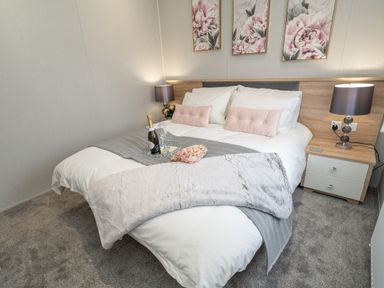 A bedroom with a bed lamps bedside table and floral paintings at Loluke Lodge on The Lake 5 Coniston Drive Borwick near Carnforth