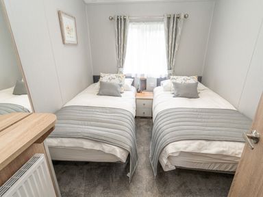 A bedroom with two single beds separated by a nightstand and a window with curtains at Loluke Lodge on The Lake 5 Coniston Drive Borwick near Carnforth
