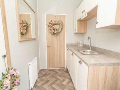 A narrow utility room with a sink countertop wooden cabinets floral wreaths on door and wall mirror at Loluke Lodge on The Lake 5 Coniston Drive Borwick near Carnforth