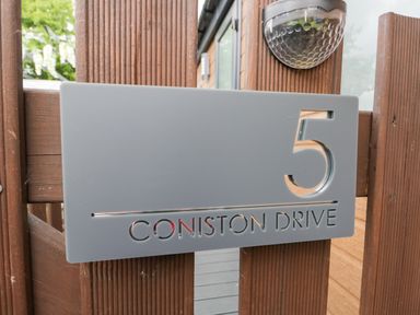 A gray house number sign with the number 5 and the text Coniston Drive mounted on a wooden gate with a black outdoor light above at Loluke Lodge on The Lake 5 Coniston Drive Borwick near Carnforth