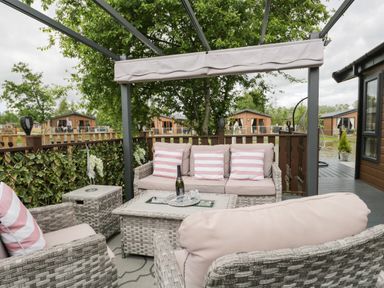 An outdoor seating area with wicker furniture and striped cushions at Loluke Lodge on The Lake 5 Coniston Drive Borwick near Carnforth