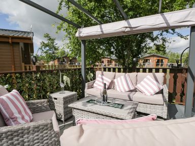An outdoor patio seating area with cushioned wicker furniture and striped pillows at Loluke Lodge on The Lake 5 Coniston Drive Borwick near Carnforth