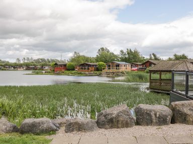 A lake with reed beds large rocks and wooden lodges on the shore at Loluke Lodge on The Lake 5 Coniston Drive Borwick near Carnforth