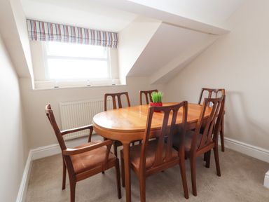 A dining area with a wooden table and six wooden chairs under a window with striped blinds at Ty Uchaf in Rhyl