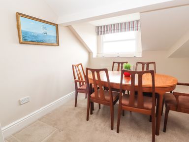 A dining room with a wooden table and six chairs a window with striped blind and a painting of a ship on the wall at Ty Uchaf in Rhyl