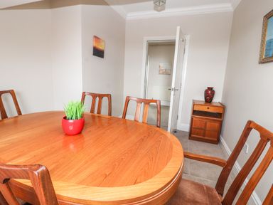 A dining room with a wooden table and chairs a red vase with green plant and a wooden cabinet with a red vase at Ty Uchaf in Rhyl