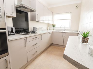 A kitchen with cabinets a gas stove a toaster kettle flowers and a plant at Ty Uchaf in Rhyl
