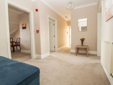 A hallway with beige carpet walls and ceiling lamp a small wooden table with flowers and a mirror above at Ty Uchaf Rhyl