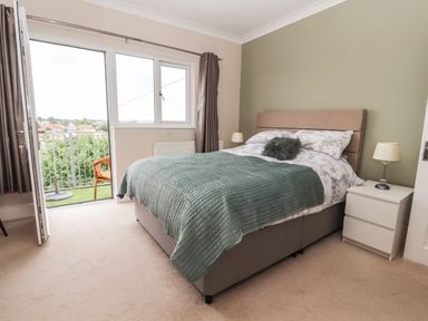 A bedroom with a bed a nightstand with a lamp an open door leading to a balcony with a chair at Ty Uchaf in Rhyl