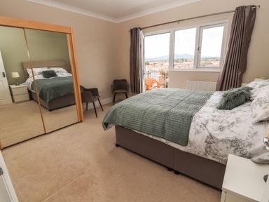 A bedroom with a bed a mirrored wardrobe two chairs and a window with curtains at Ty Uchaf in Rhyl