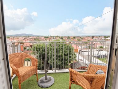 A balcony with two wicker chairs and an umbrella stand overlooking rooftops and hills at Ty Uchaf in Rhyl