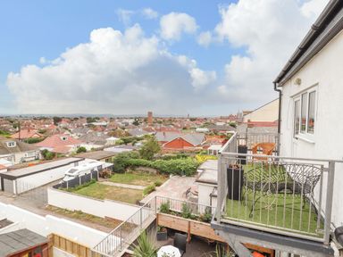 A balcony with chairs overlooking a residential neighborhood with houses and gardens at Ty Uchaf in Rhyl