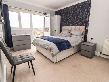 A bedroom with a double bed bedside tables a chair a chest of drawers and a door leading to a balcony at Ty Uchaf in Rhyl