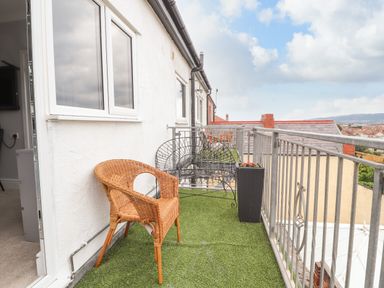 A balcony with a wicker chair a metal bench and a planter with flowers at Ty Uchaf in Rhyl