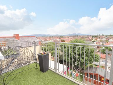 A balcony with a metal bench and potted plant overlooking rooftops and mountains at Ty Uchaf in Rhyl